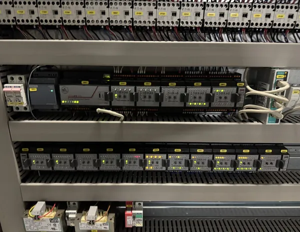 Blick in einen geöffneten Schaltschrank: Automationsstation mit Ein- und Ausgangsmodulen und Status-LEDs, darüber Schützreihen, sauber beschriftete Klemmen und Verdrahtung